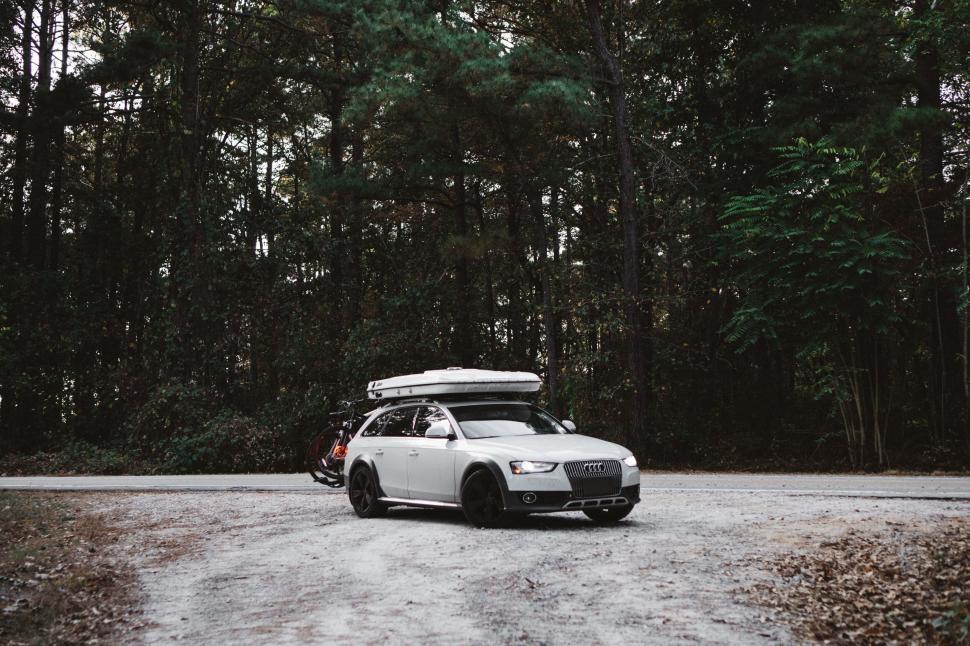 Free Image of Car parked on a dusty road next to forest 