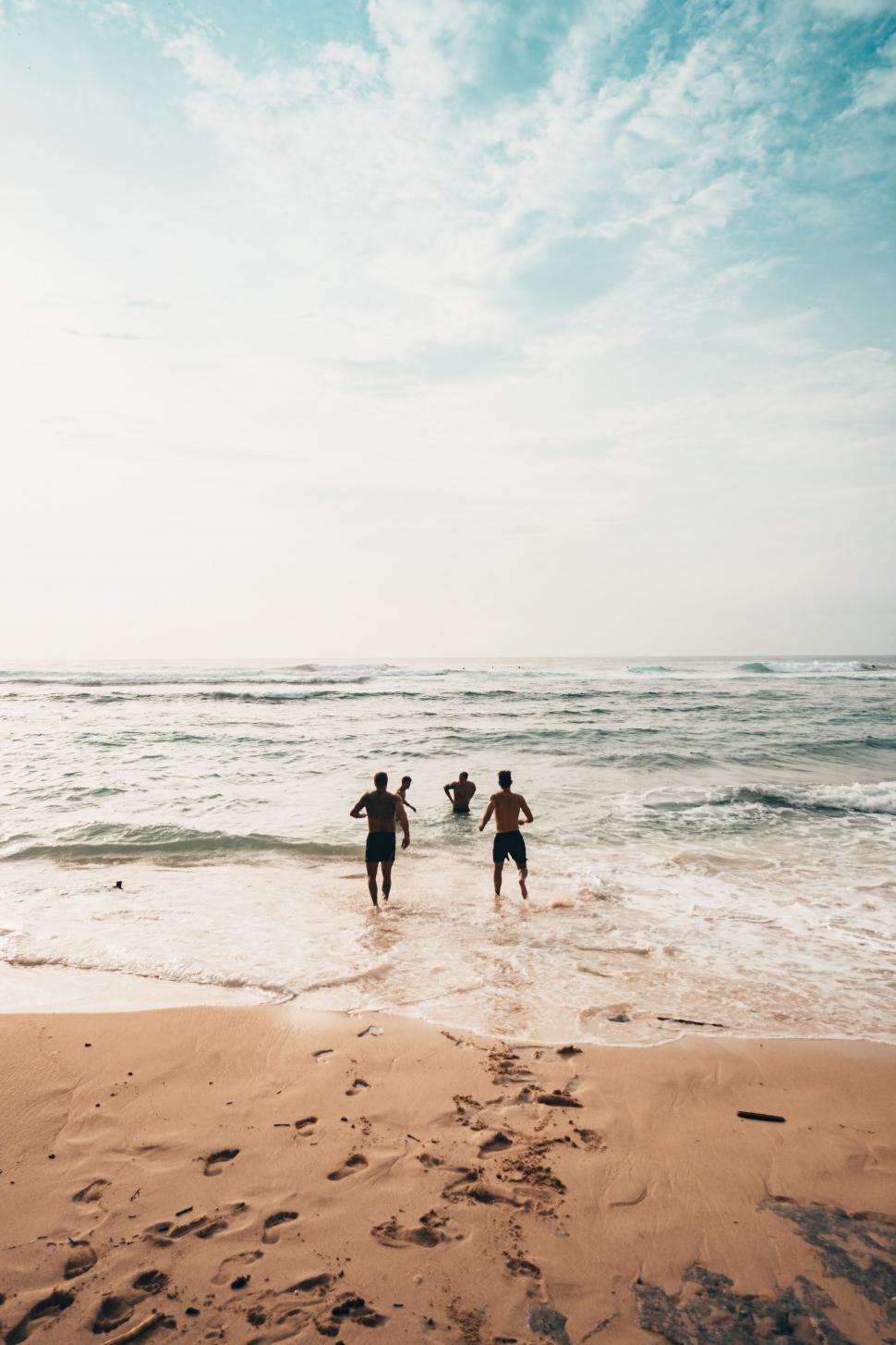 Free Image of Friends running towards the ocean at the beach 