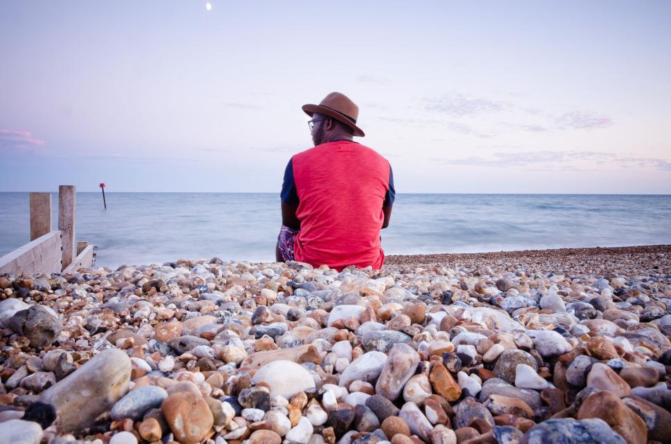 Free Image of Man sitting on pebble beach looking at sea 