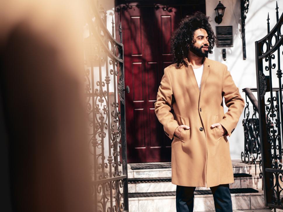 Free Image of A man with long curly hair wearing a coat and standing in front of a door 