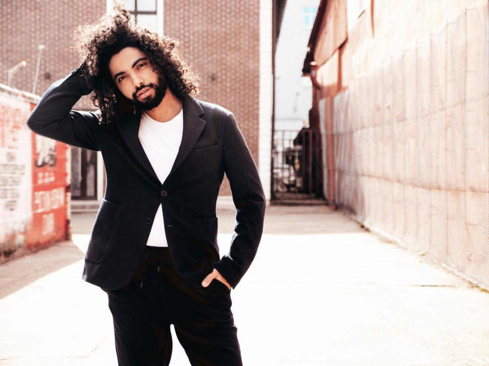 Free Stock Photo of A man with long curly hair and beard wearing a black  suit