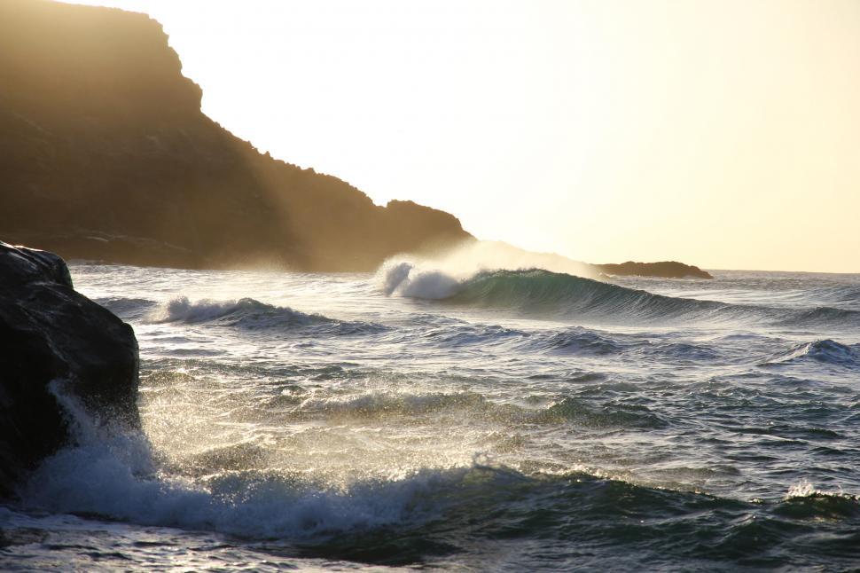 Free Image of Sunset waves crashing against rocks 