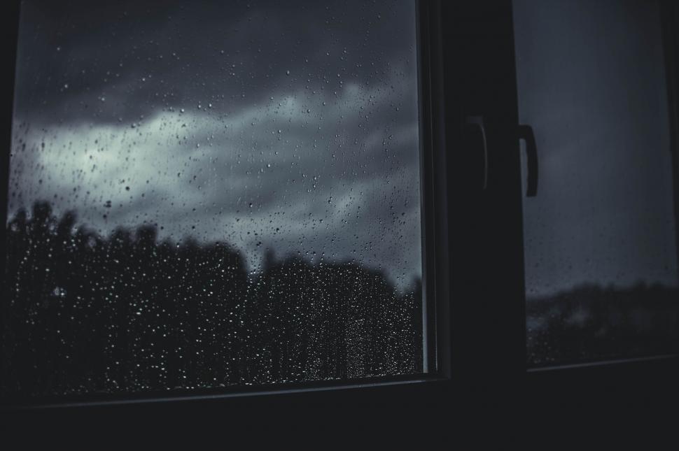 Free Image of Raindrops on window with dark cloudy sky 