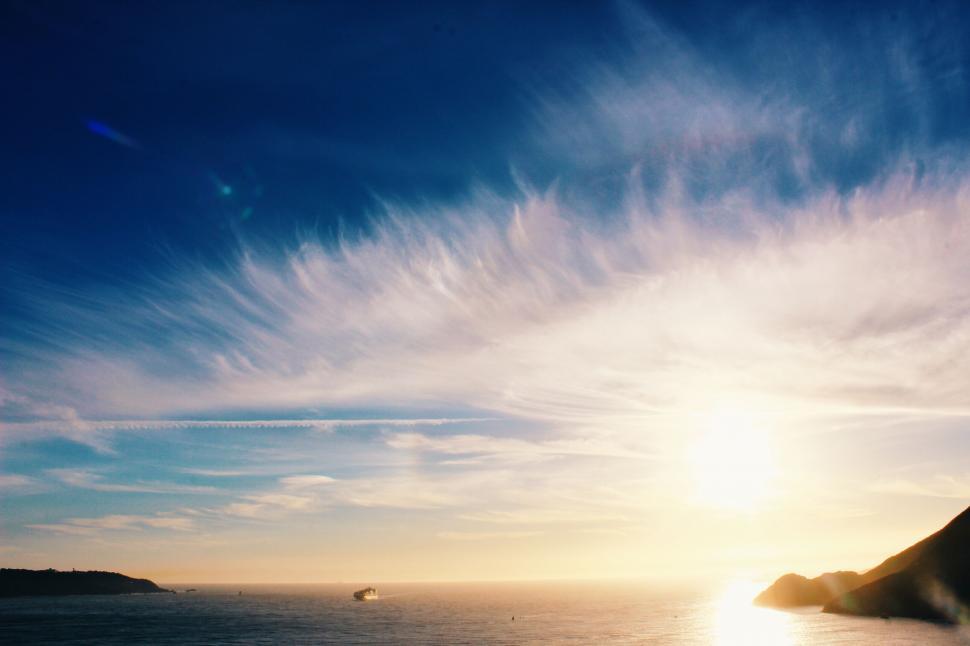 Free Image of Sunset over the ocean with silhouetted hills 