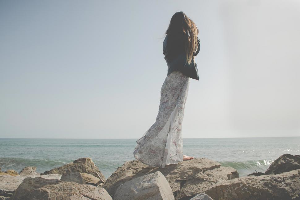 Free Image of Woman standing on rocks by the ocean 