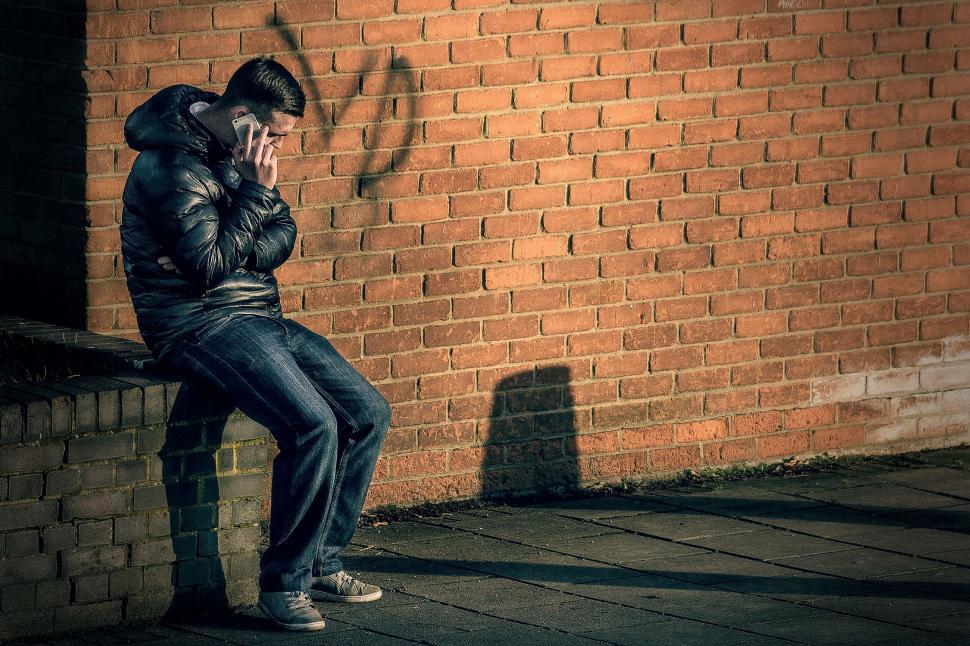 Free Image of Person sitting by a brick wall 
