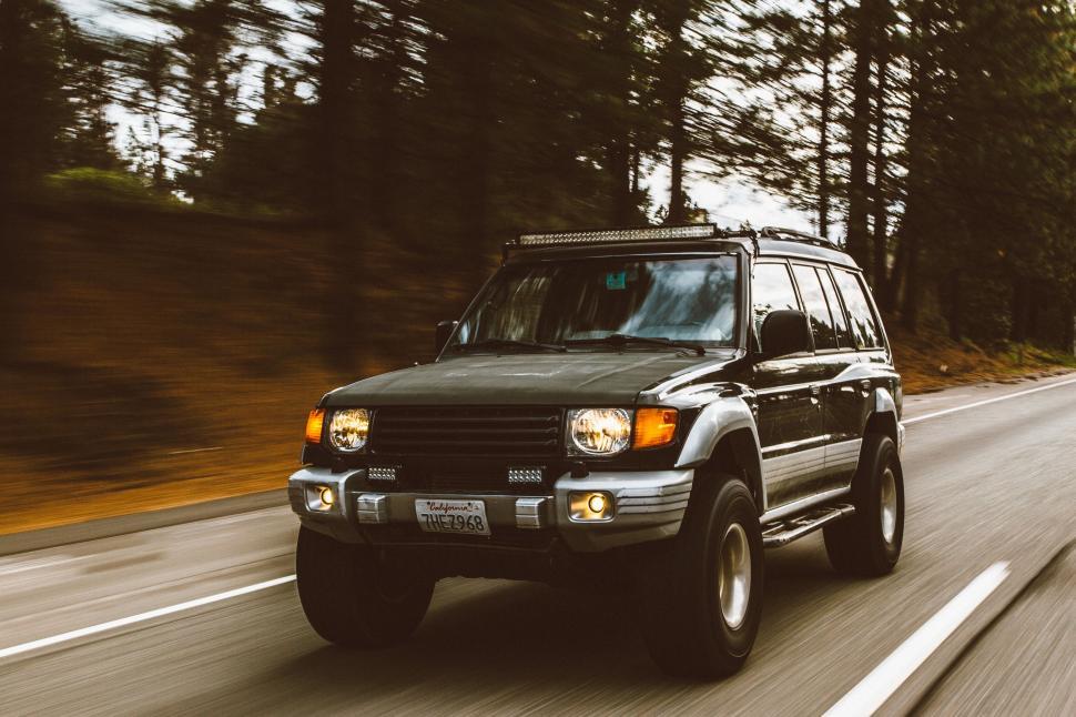 Free Image of SUV moving on roadway surrounded by trees 