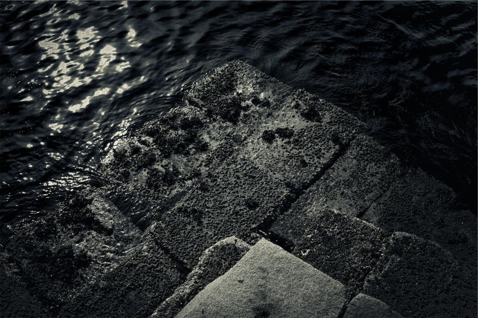 Free Image of Dark textured stones by water s edge 