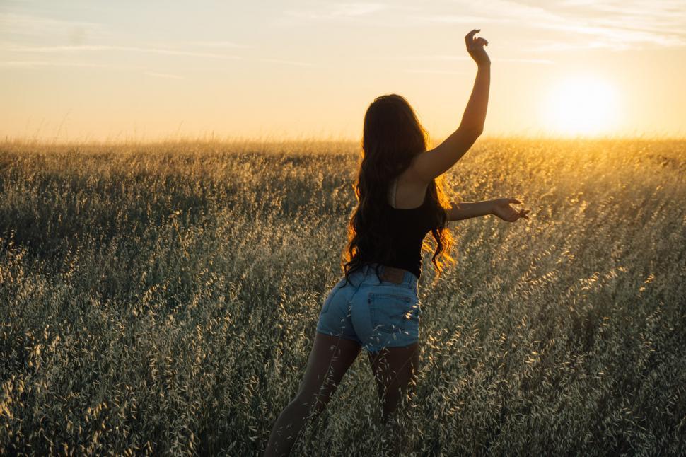 Free Image of Woman in a field at sunset feeling free 