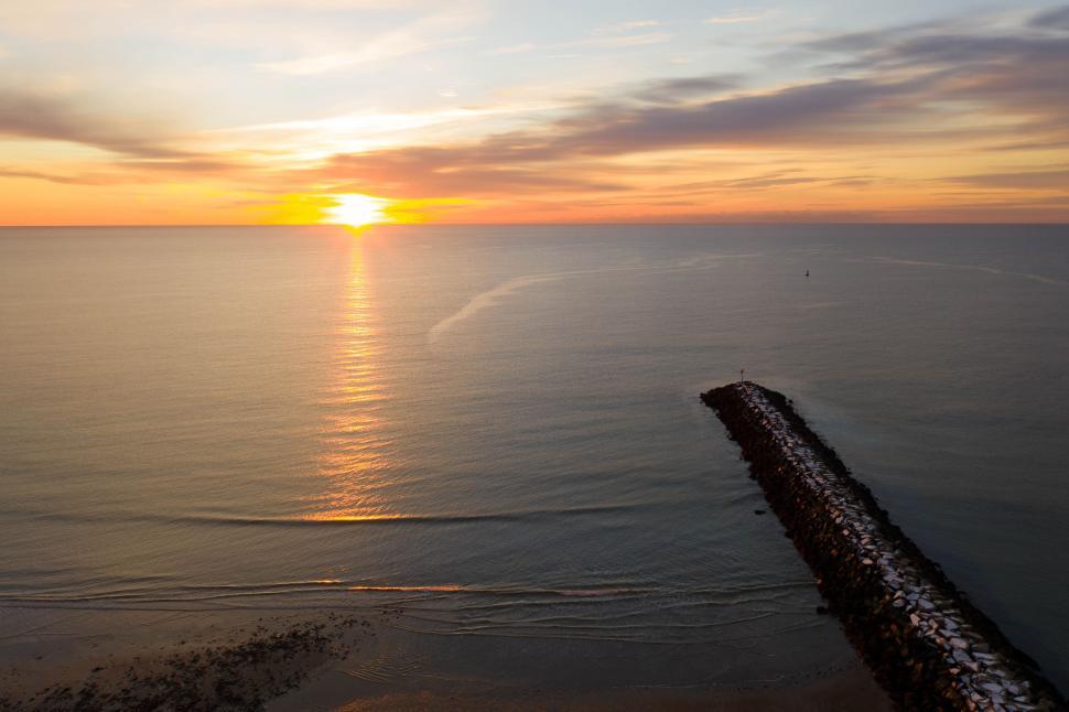Free Image of Sunset over ocean with jetty extending into water. 
