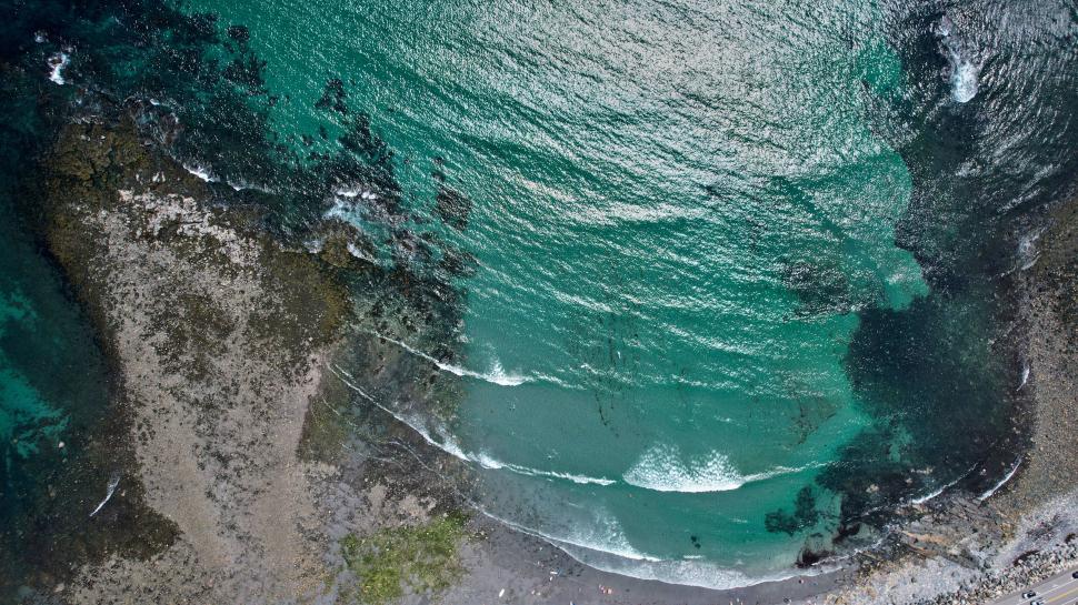 Free Image of Aerial view of green ocean waves hitting rocky shore. 
