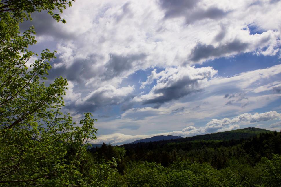 Free Image of Lush green landscape under dramatic cloudy blue skies 