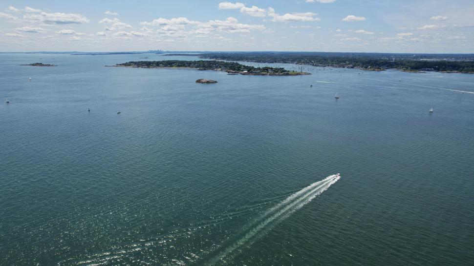 Free Image of Boat leaving a trail on calm blue sea, bright sky 