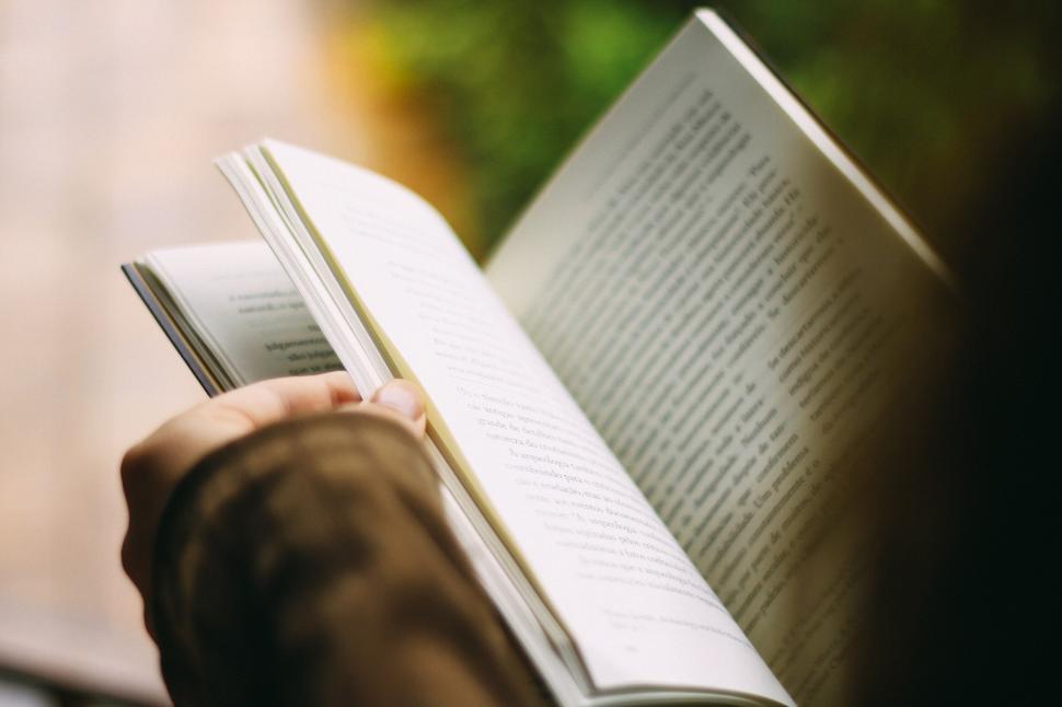Free Image of Hands holding and reading an open book close up outdoors. 