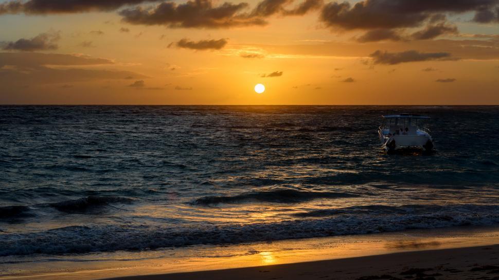 Free Image of Sunset over the ocean with a boat anchored near shore 