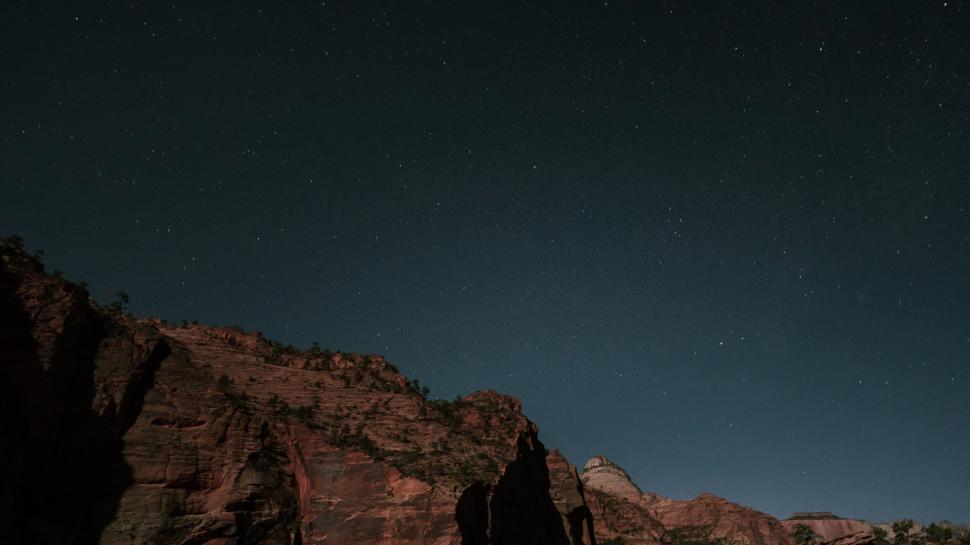 Free Image of Starry night sky above red rocky desert landscape 