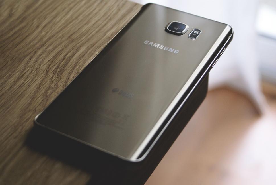Free Image of Samsung smartphone on a wooden table with glossy finish 