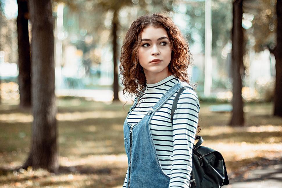 Free Image of Person in denim overalls standing on a park pathway 