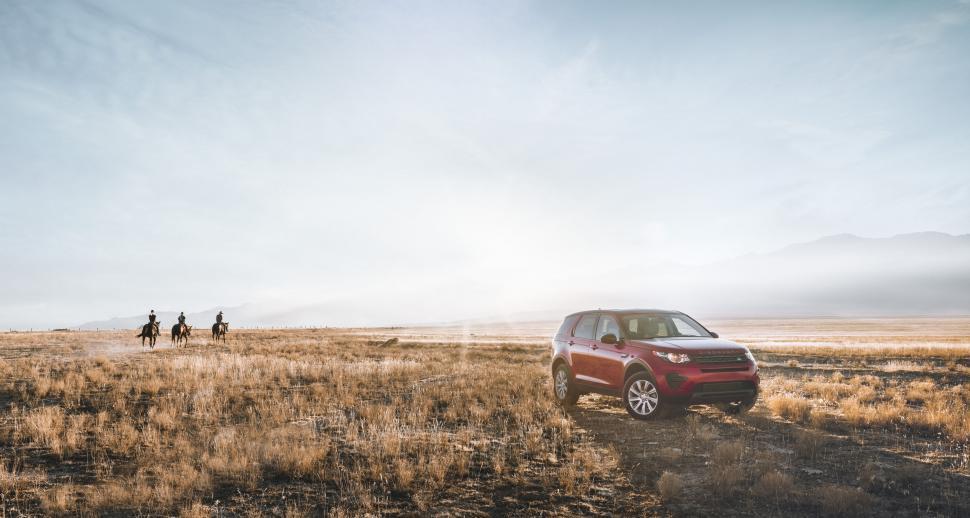 Free Image of Red SUV in expansive dry plain with horse riders 