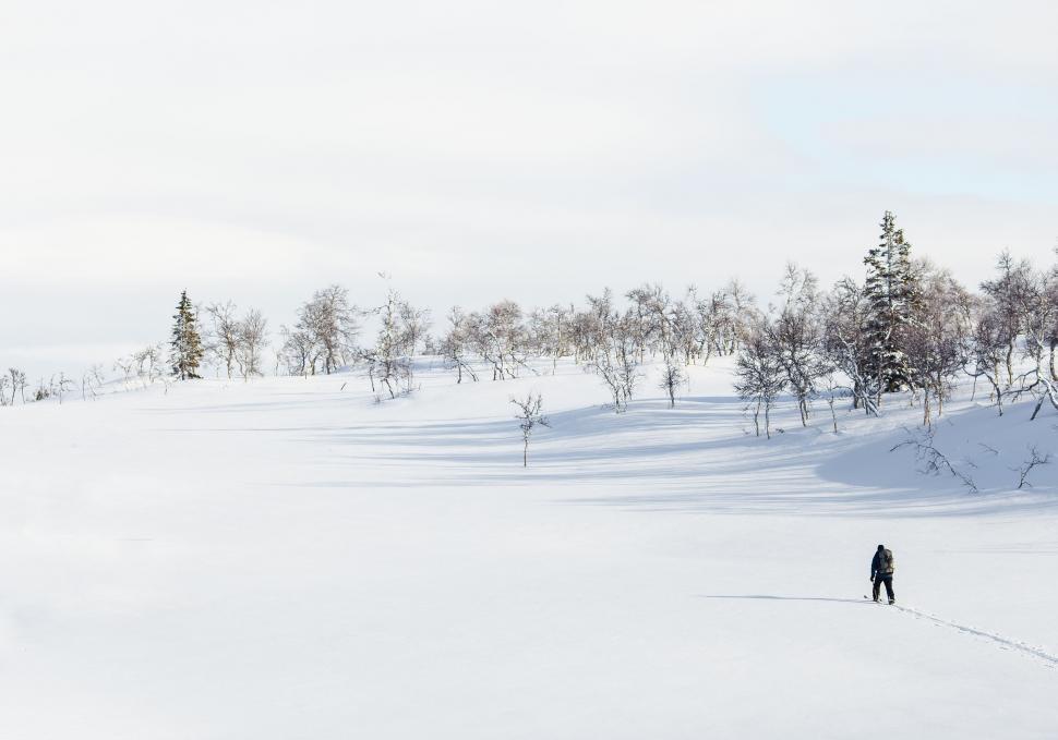 Free Image of Lone figure trekking through snowy landscape under sky 