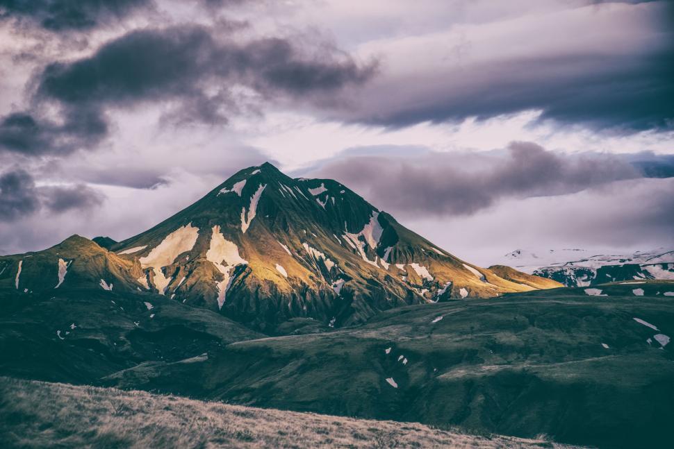 Free Image of Mountain with snow patches and green grass, dark sky. 