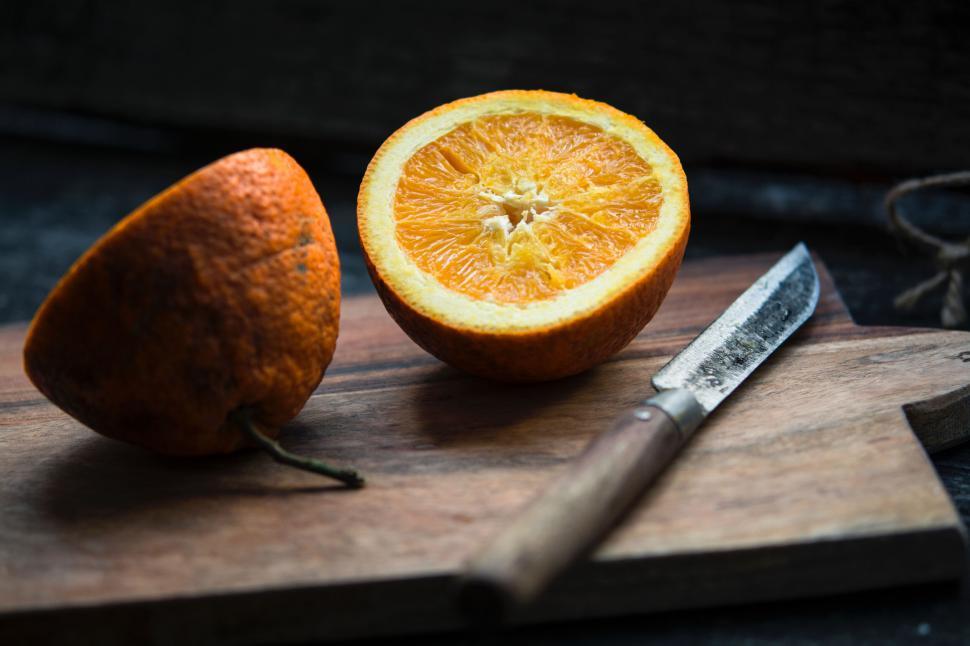 Free Image of Orange cut in half on a wooden board with knife 
