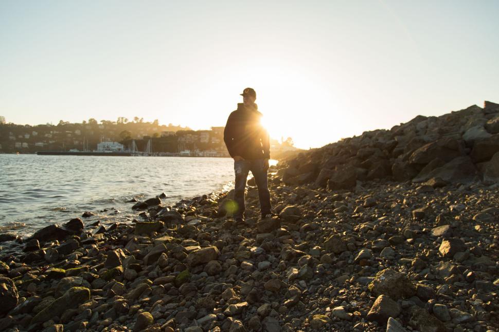 Free Image of Person on rocky beach with golden sunset on the horizon 