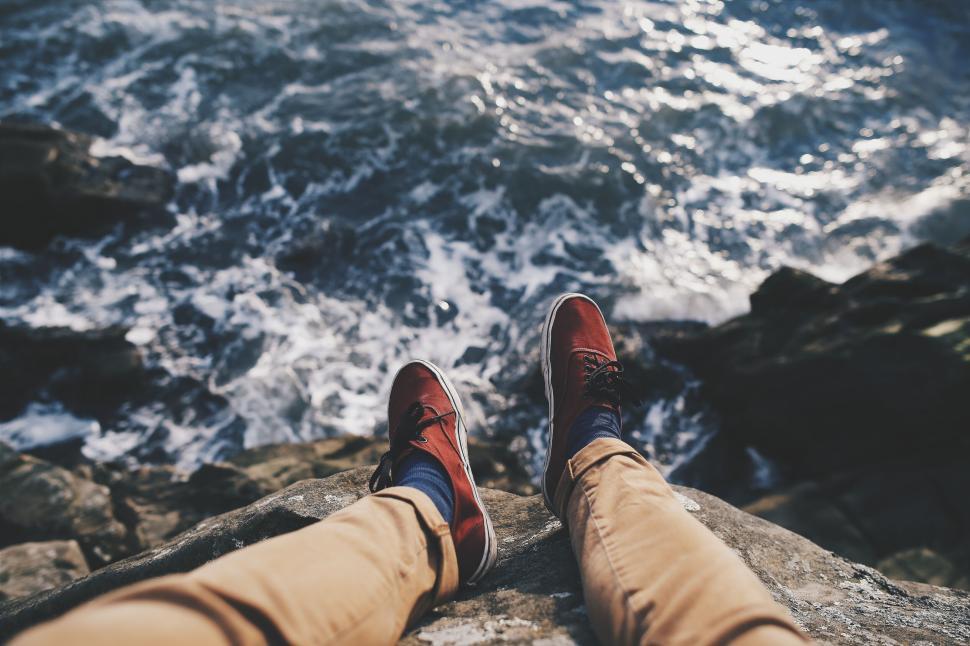 Free Image of Person s feet dangling over rocky ocean shore. 