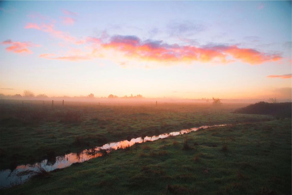 Free Image of Rainbow colored sky over dawn lit open fields and stream 
