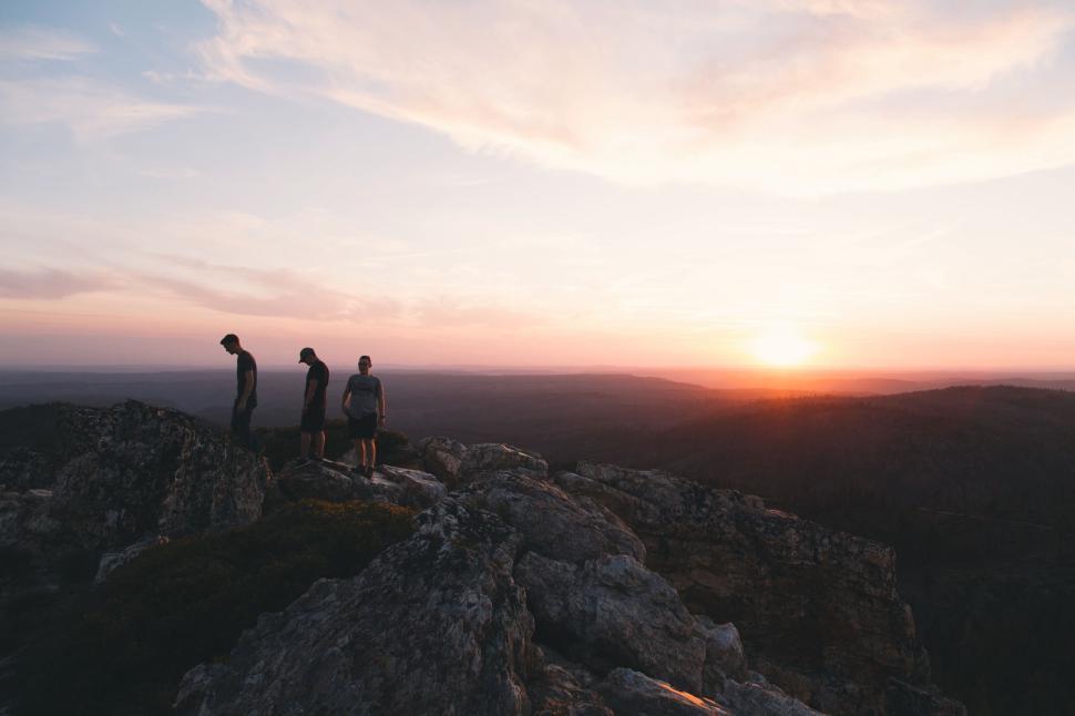 Free Image of Three hikers atop rocky cliff at sunset overlooking valley 