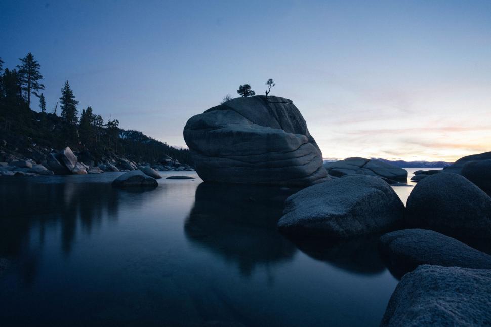 Free Image of Large boulder surrounded by calm lake at twilight hour 