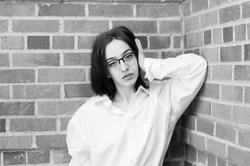Free Image of Serious woman in glasses leans against a brick wall. 