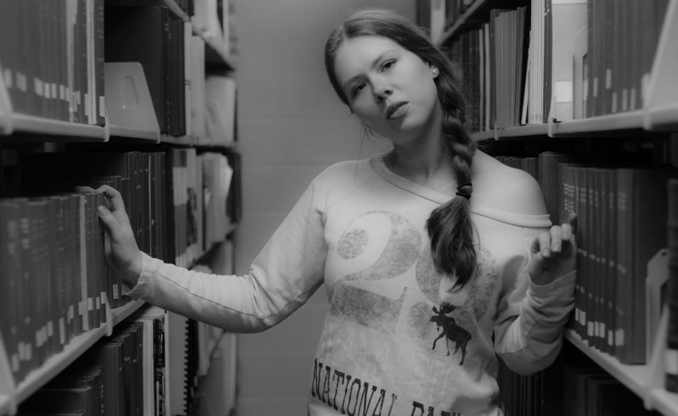Free Image of Black and white photo of woman standing in library aisle. 