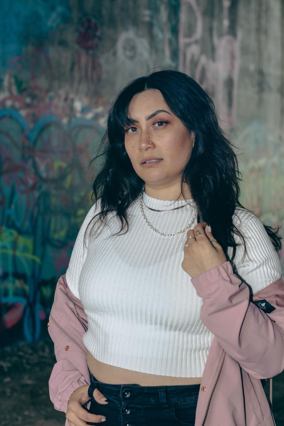 Free Image of Woman standing in front of graffiti wall, confident pose 