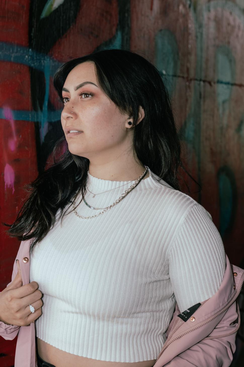 Free Image of Person in white top with pink jacket and graffiti wall 