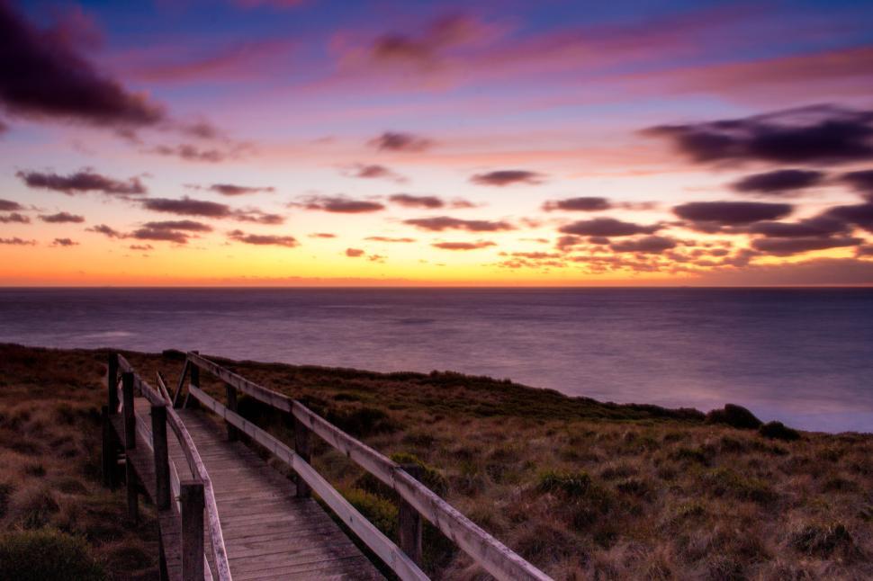 Free Image of Scenic sunset view with a wooden pathway by the ocean. 