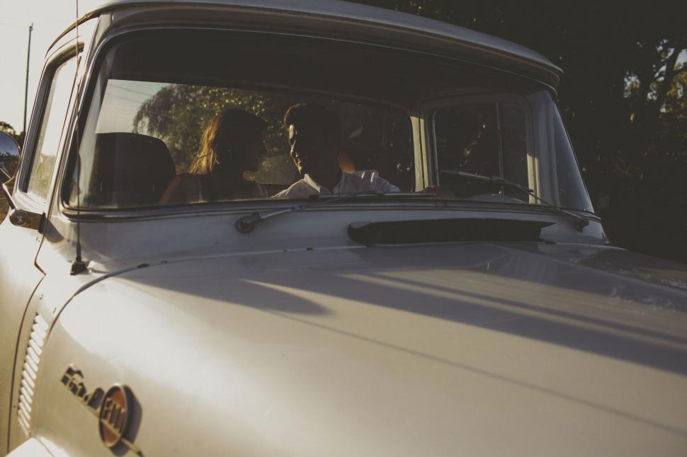 Free Image of Couple sitting in a classic car with sunlight shining. 