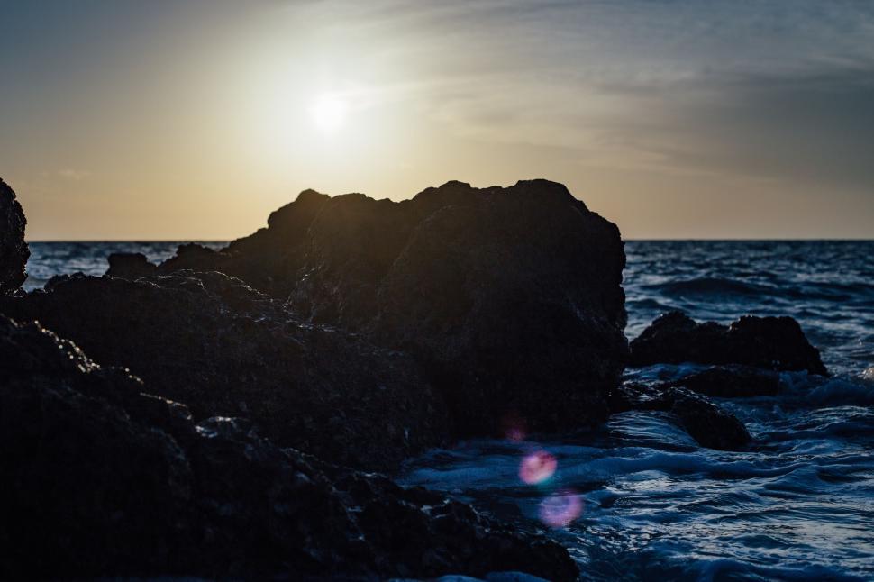Free Image of Silhouetted rocks against a setting sun and ocean waves 