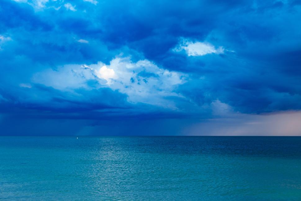 Free Image of Blue ocean with dramatic clouds overhead, serene view 