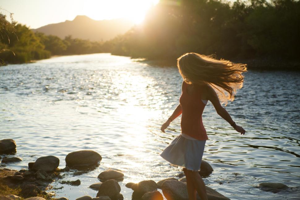 Free Image of Woman spinning by river at sunset creating a silhouette 