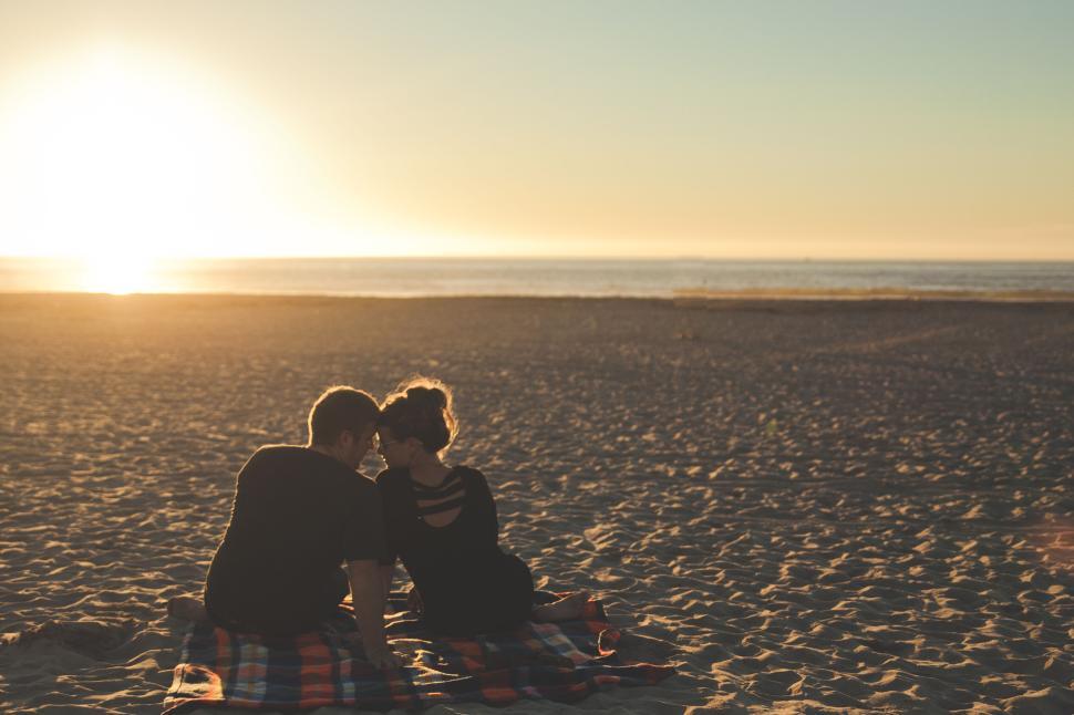 Free Image of Couple sitting on a beach blanket at sunset together 