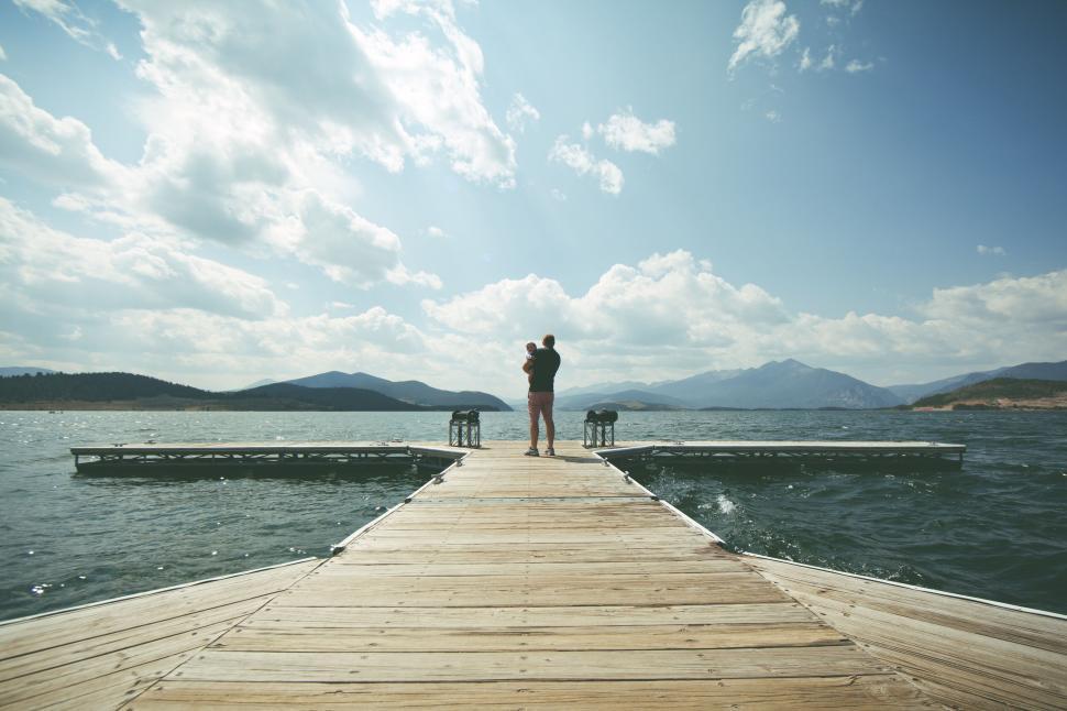 Free Image of Person holding child standing on dock over calm lake. 
