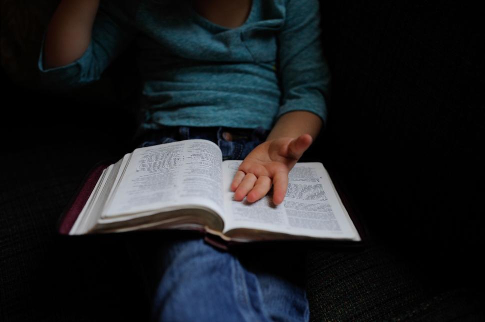 Free Image of Child reading a book with focus on hand turning pages 