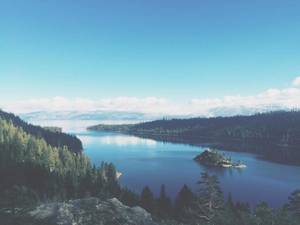 Free Image of Tranquil lake surrounded by trees under clear blue sky. 