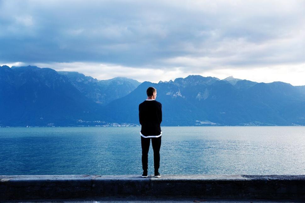 Free Image of Person on a ledge overlooking a vast mountainous lake. 
