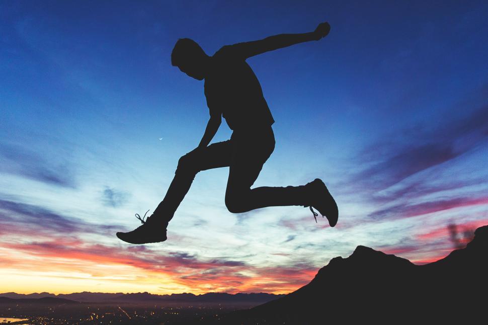Free Image of Silhouetted jumper at sunset with colorful horizon sky. 