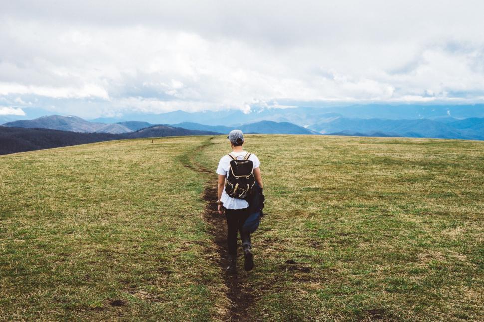 Free Image of Hiker in the expansive, green field with mountains in the background. 