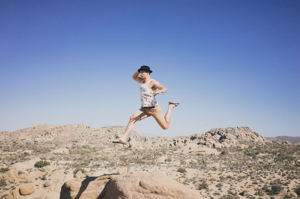 Free Image of Person jumping in desert with rocks under clear blue sky. 