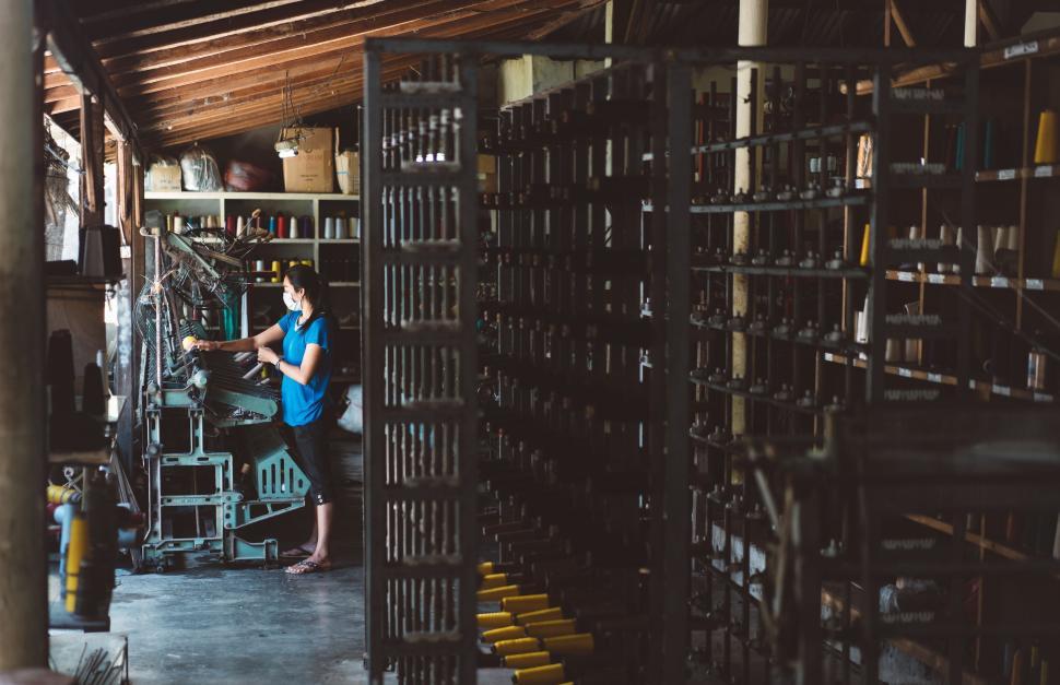 Free Image of Woman working in textile factory surrounded by machinery and yarn 