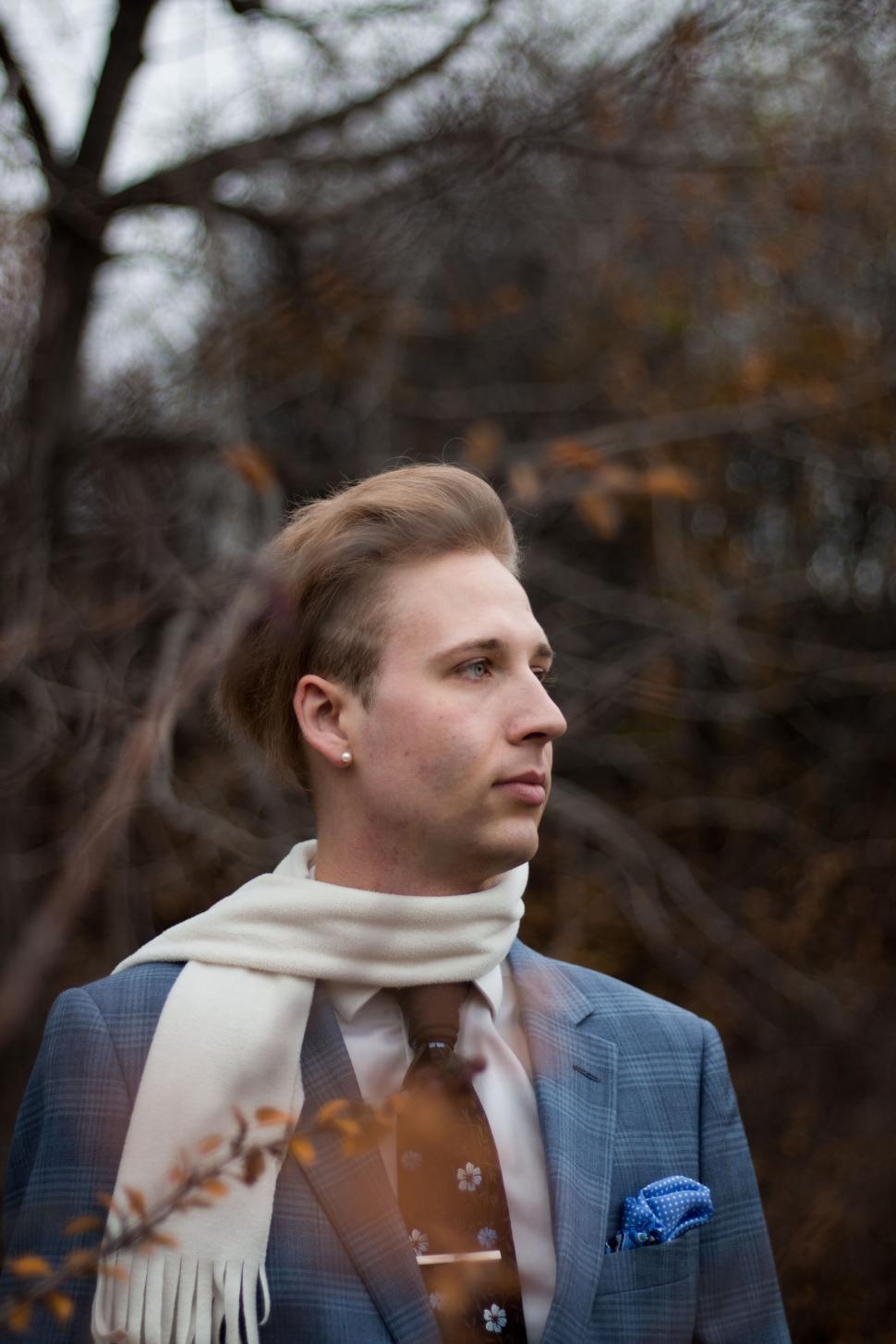 Free Image of Stylish person in blue suit and white scarf stands in forest setting. 